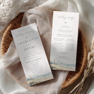 May include: Two vertical wedding ceremony programs printed on white cardstock with black serif and script typography. The bottom of each card features a watercolor illustration of a sandy beach with dune grass and blue ocean waves.