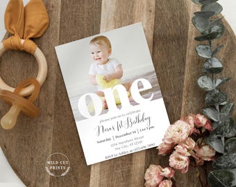 Puede incluir: Una tarjeta blanca con la palabra "one" en letras grandes, negritas y blancas. La tarjeta tiene una foto de una niña pequeña con un vestido blanco y una manta amarilla. El texto de la tarjeta dice "Por favor, únase a nosotros para celebrar el primer cumpleaños de Nora, sábado 14 de diciembre, de 1 a 3 pm, 1234 Anywhere Street, Any City, ST 12345, RSVP a Ashley al (123)456 7890."