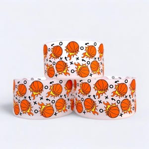 May include: Three light pink ceramic bowls with a basketball theme. Each bowl is decorated with orange basketballs, flames, and black and white graphic elements. The bowls are stacked in a triangular arrangement.