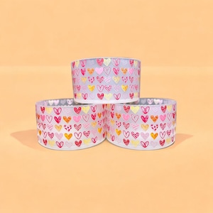 May include: Three clear glass containers with a pink, red, and yellow heart pattern. The containers are stacked on top of each other.