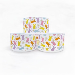 May include: Three white ceramic bowls with a pattern of colorful pastel bunnies and white flowers.