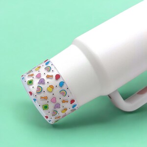 May include: White insulated bottle with a colorful patterned lid. The lid features a repeating pattern of rainbows, hearts, stars, and other small shapes in various colors.