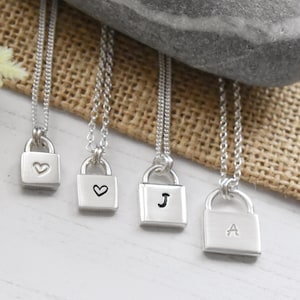 May include: Four silver lock necklaces with different charms. One charm has a heart, one has a heart with a small letter J, and one has a letter A.