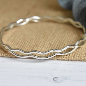 May include: A silver bangle bracelet with a wavy design. The bracelet is made of two thin bands of metal that are intertwined.