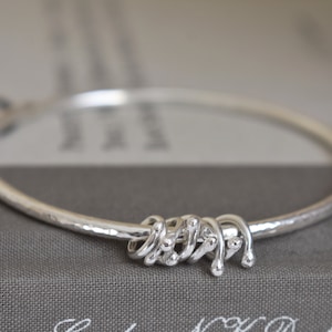 May include: A silver bangle bracelet with a hammered finish and a knot design. The knot is made of multiple small, rounded silver pieces.