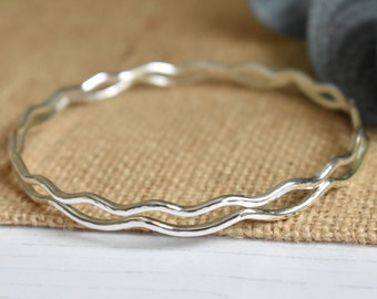 May include: A silver bangle bracelet with a wavy design. The bracelet is made of two thin bands of metal that are intertwined.
