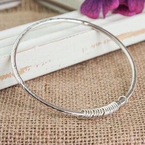 May include: A silver bangle bracelet with a hammered finish and a coiled wire detail.