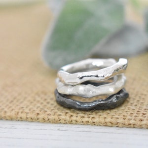 May include: Three silver rings stacked on top of each other. The top two rings are smooth and the bottom ring is textured.