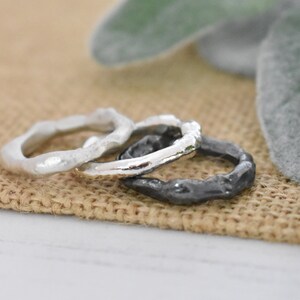 May include: Three silver rings with a textured, organic design. The rings are stacked on top of each other, with the largest ring on the bottom and the smallest ring on top.