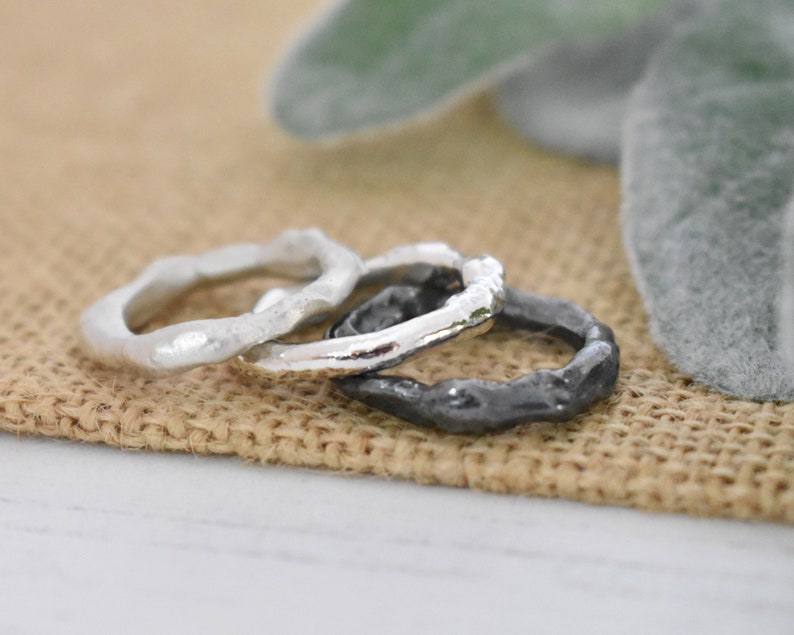 May include: Three silver rings with a textured, organic design. The rings are stacked on top of each other, with the largest ring on the bottom and the smallest ring on top.