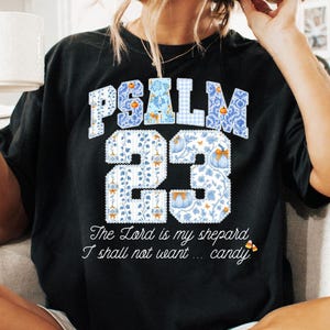 May include: Black t-shirt with the text "PSALM 23" in a blue floral design. The shirt also features the quote "The Lord is my shepherd, I shall not want... candy."