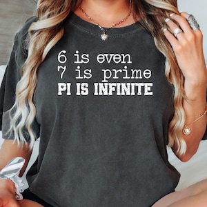May include: Dark gray t-shirt with white text: "6 is even, 7 is prime, PI IS INFINITE." The shirt has short sleeves and a crew neck. The text is in a bold, sans-serif font.