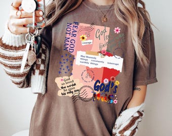 May include: A brown t-shirt with a graphic design featuring the text "FEAR GOD NOT MAN" and other religious phrases. The design includes floral accents and a collage of text elements. The shirt is a casual, unisex style.