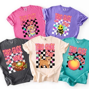 Puede incluir: Cinco camisetas de manga corta en rosa, morado, gris oscuro, crema y verde azulado. Cada camiseta presenta un cuadrado a cuadros en blanco y negro con el texto "THIRD GRADE IS THE" y un gráfico de un gato, una abeja, un burrito o un melocotón.