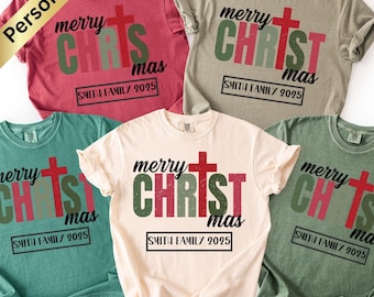 May include: A collection of five t-shirts in various colors, including red, green, and beige. Each shirt features the text "merry CHRISTmas" with a cross design and "SMITH FAMILY 2025" in a black rectangle. A gold banner reads "Personalize".