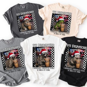 Könnte beinhalten: Fünf T-Shirts in Anthrazit, Creme, Grau, Weiß und Schwarz mit einer Grafik eines Tieres mit Weihnachtsmütze und Headset, das vor einem Krankenwagen Eiskaffee trinkt. Der Text lautet 911 DISPATCHER CAFFEINATED CHRISTMAS CHAOS IS KINDA MY THING.