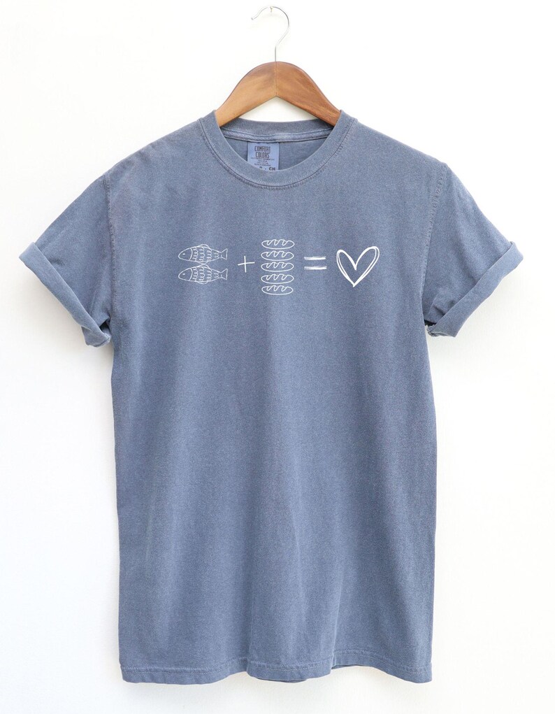 May include: A blue t-shirt with rolled-up sleeves. The shirt features a white graphic of two fish, bread, and a heart symbol. The design suggests a love for fish and bread.