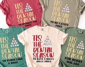 Könnte beinhalten: Fünf T-Shirts in verschiedenen Farben, jeweils mit dem Text "Tis the Dental Season" und einem Weihnachtsbaum aus Zähnen. Die Shirts haben verschiedene Slogans: "To Sparkle and Shine", "To Be Cavity Free", "To Floss Like a Boss", "To Have a Holly Jolly Smile" und "For Merry Molars".