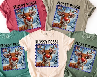 Könnte beinhalten: Fünf T-Shirts in verschiedenen Farben, darunter Rot, Grün und Beige. Jedes Shirt zeigt eine Grafik eines Rentiers mit roter Nase und dem Text "FLOSSY POSSE" in Schwarz. Das Rentier ist vor einer verschneiten Winterlandschaft platziert.