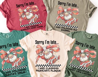 Könnte beinhalten: Fünf verschiedenfarbige T-Shirts mit einem Weihnachtsmann-Motiv. Jedes Shirt trägt den Text "Sorry I'm late..." und einen anderen zahnmedizinischen Satz, wie "I was diagnosing candy cane cavities."