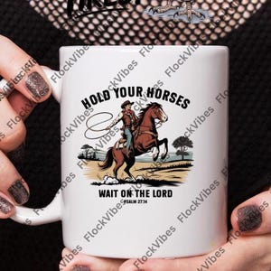 Könnte beinhalten: Eine weiße Keramiktasse mit einem Cowboy, der ein Pferd reitet und ein Lasso hält. Der Text auf der Tasse lautet "Hold Your Horses Wait On The Lord Psalm 27:14".