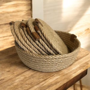 May include: A round jute basket with matching coasters. The basket and coasters are a natural tan colour, with brown leather accents on the coasters and basket rim. Coasters are stacked inside the basket.