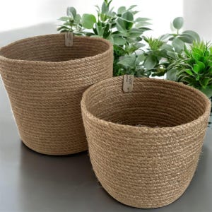 May include: Two brown jute rope plant pots, one larger than the other, with a brown paper tag that says "MADE WITH LOVE" on the larger pot.
