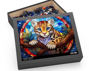 May include: A 500 piece jigsaw puzzle featuring a colorful stained glass style illustration of an ocelot. The ocelot is perched on a branch with a blue, green, and red background. The puzzle box is black with the text "16x20 Puzzle 500 pcs Ages 9+"