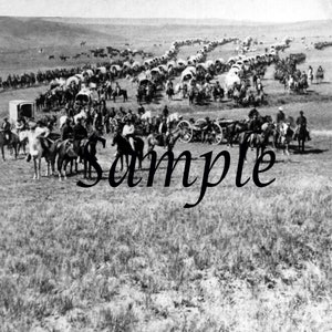 Peut inclure: Une photographie en noir et blanc d'un grand groupe de personnes à cheval, voyageant en ligne droite à travers une plaine herbeuse. Les personnes sont vêtues de vêtements d'époque et transportent des provisions sur leurs chevaux. L'image est une représentation historique d'un train de chariots.
