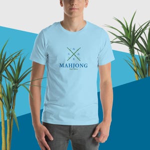Puede incluir: Una camiseta azul claro con un diseño de bambú verde y el texto "Mahjong Your Move" en azul.