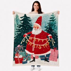 May include: A rectangular throw blanket featuring a watercolor-style illustration of Santa Claus in a red coat and hat, holding a banner that reads HAPPY CHRISTMAS. The scene includes dark green pine trees, falling snow, and colorful gift boxes.
