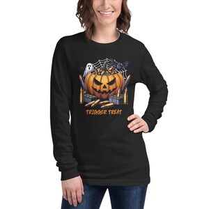 Peut inclure: T-shirt noir à manches longues avec un motif d'Halloween. Le motif représente une citrouille orange remplie de balles, un fantôme, une chauve-souris et le texte "Trigger Treat" en orange.