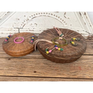 May include: Two round woven baskets with lids, decorated with colorful beads and coins. The baskets are made of natural materials and have a rustic, vintage look.