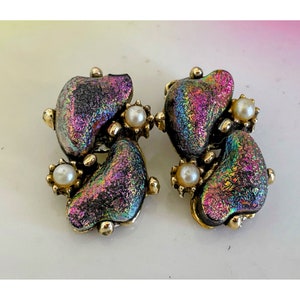 May include: A pair of vintage earrings with a gold-tone setting. Each earring features a dichroic glass stone with iridescent purple, green, and gold hues, accented by a small faux pearl and gold-tone floral details.
