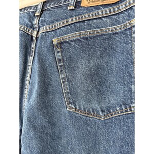 Puede incluir: Vaqueros de mezclilla azul oscuro con un dise&ntilde;o cl&aacute;sico de cinco bolsillos y costuras doradas visibles. En la cintura hay una etiqueta de cuero beige con el texto Wrangler Authentic Jeans impreso en tinta negra sobre la superficie.