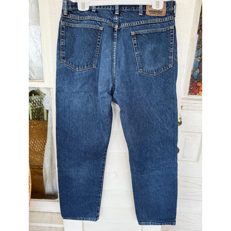 Puede incluir: Un par de vaqueros de mezclilla azul oscuro con un dise&ntilde;o cl&aacute;sico de cinco bolsillos, cierre de bot&oacute;n y cremallera, y trabillas para cintur&oacute;n. Un parche de cuero color canela con la marca Wrangler est&aacute; cosido en la cintura trasera.