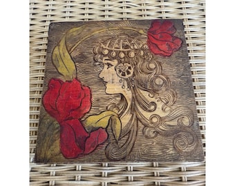 May include: Wooden art piece featuring a profile of a woman with long, curly hair and ornate headwear. Two red flowers with yellow leaves frame the woman's face. The artwork is carved into a square wooden panel.