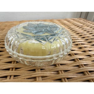 May include: A clear glass trinket box with a cut glass design. The lid features a raised, frosted glass floral design.