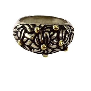 May include: A silver ring with a floral design and gold accents. The ring has a wide band and is decorated with a repeating pattern of stylized flowers. Small gold spheres are placed around the ring.