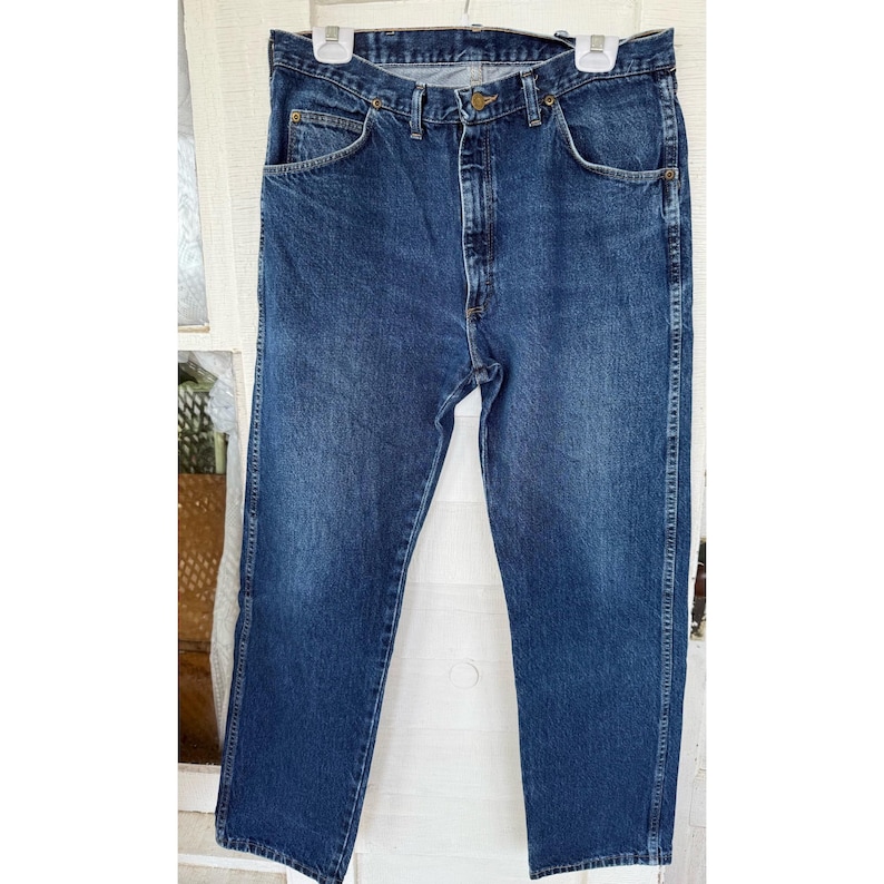 Puede incluir: Un par de pantalones vaqueros de mezclilla azul oscuro con un dise&ntilde;o cl&aacute;sico de cinco bolsillos, cierre de bot&oacute;n met&aacute;lico en la cintura, cremallera y remaches visibles de color cobre en las esquinas de los bolsillos. Tela con lavado uniforme.