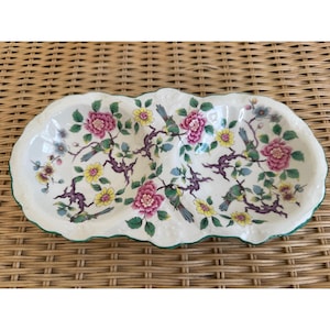 May include: A white porcelain serving dish with a green rim and a floral design featuring pink and yellow flowers, green leaves, and birds. The dish is divided into two sections.