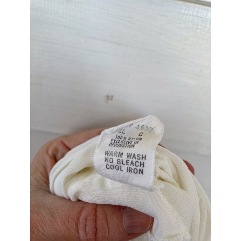 Op de afbeelding: Wit waslabel met zwarte tekst die luidt: "100% Nylon Exclusief van decoratie Warm wassen Niet bleken Koel strijken"