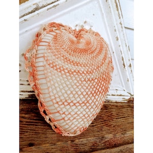 May include: A crocheted heart-shaped pillow with a white and orange ombre design. The pillow is made with a delicate openwork stitch.