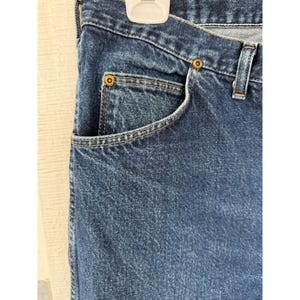 Puede incluir: Vaqueros de mezclilla azul oscuro con una construcci&oacute;n cl&aacute;sica de cinco bolsillos que incluye un bolsillo para monedas, remaches met&aacute;licos de color cobre en los puntos de tensi&oacute;n, cintura resistente con trabillas y costuras en contraste naranja.