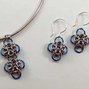 Può includere: Una collana a catena d'argento con un ciondolo con due ciondoli a forma di fiore blu e argento. Sono inclusi anche orecchini abbinati con un singolo ciondolo a forma di fiore blu e argento.