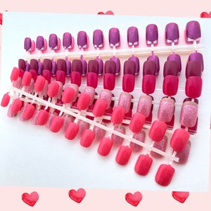 Bundle of 10 petite active sets of press on nails in neon pink, rose glitter, magenta and other pink shades rest on a white background. pink frame with red hearts surrounds the image.