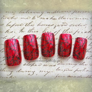 5 red square false fingernails with black geometric detailing rest on a beige paper with old fashioned script. There is a textured beige frame around the image.