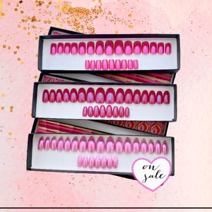 Three rectangular boxes contain sets of pink press on nails in square, oval and stiletto shapes on a pink background with gold splash detail. white heart graphic on lower left reads on sale in black text.