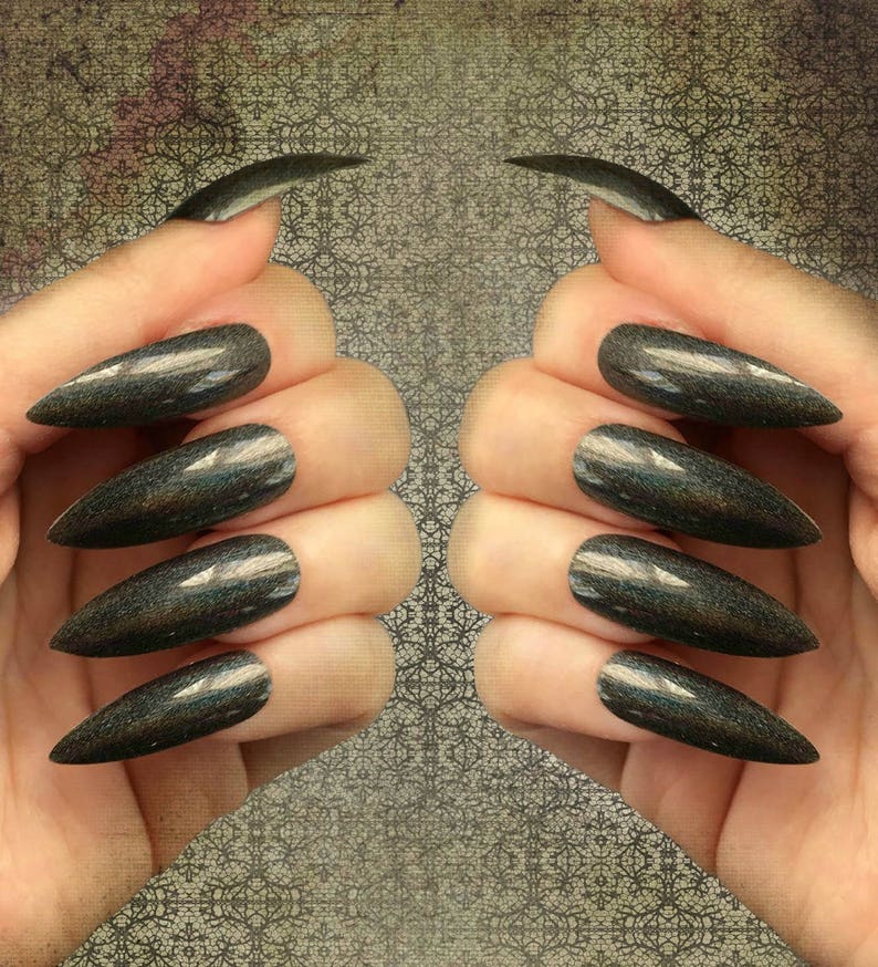 White female left and right hand wearing long black holographic stiletto press on nails on a textured gray background.