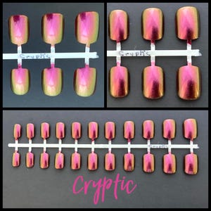 K&ouml;nnte beinhalten: Ein Set mit 20 falschen N&auml;geln mit holografischem Finish. Die N&auml;gel sind eine Mischung aus Pink und Gr&uuml;n mit einem schimmernden Effekt. Die N&auml;gel sind auf einem wei&szlig;en Plastikstreifen angeordnet, auf dem das Wort "Cryptic" gedruckt ist.